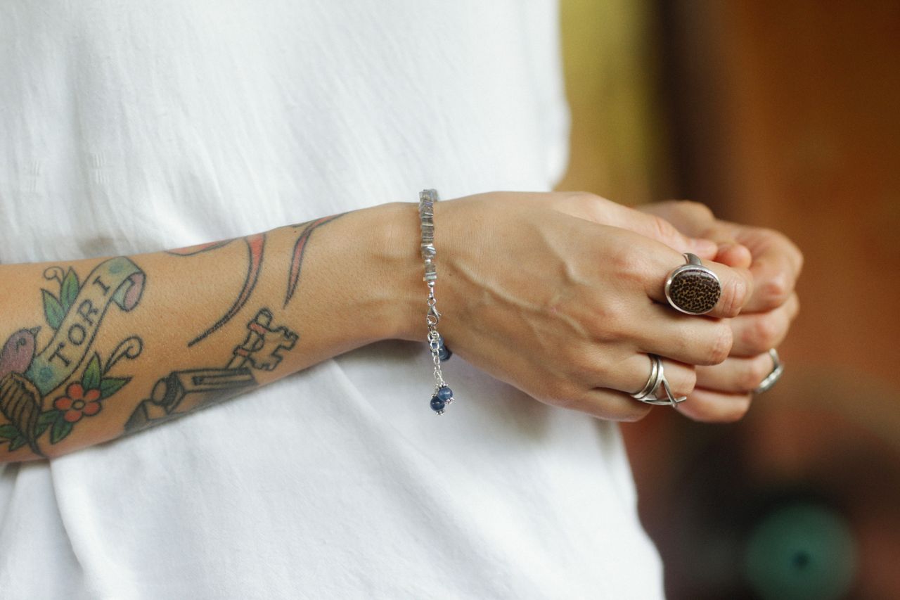 Close-up of a tattooed arm adorned with bracelets and rings, showcasing personal style.