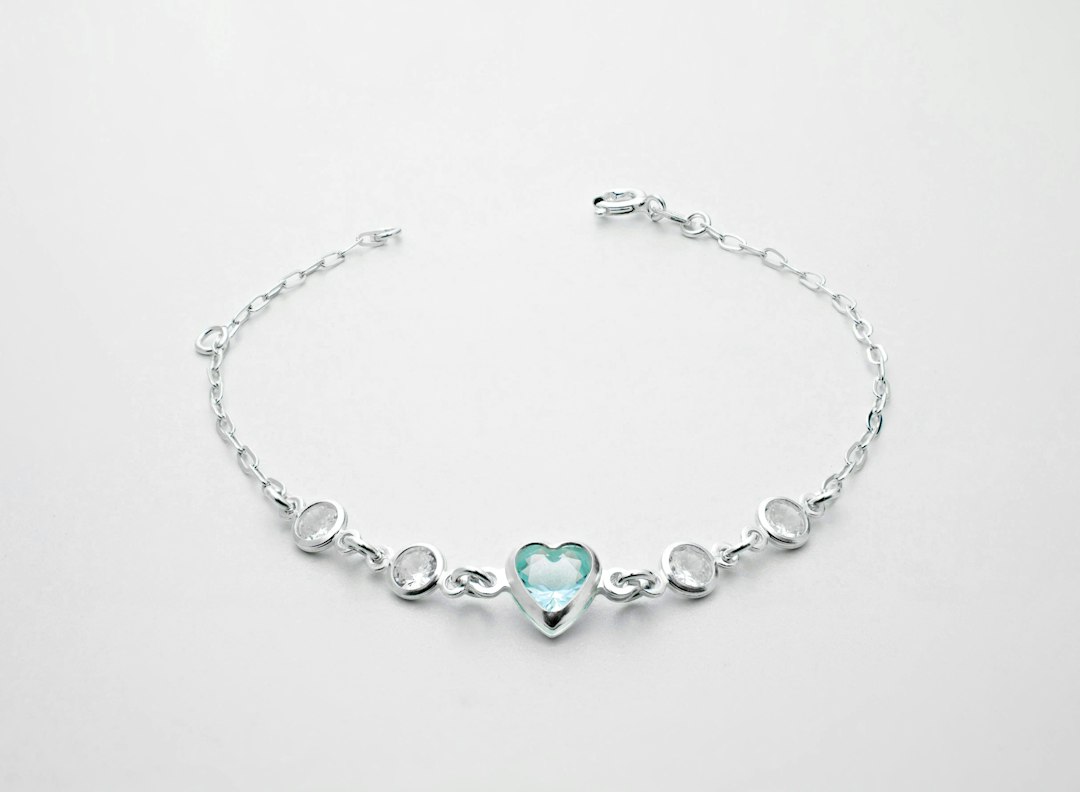 Front view of a beautiful silver bracelet with a green heart-shaped gemstone on top of a clean white surface